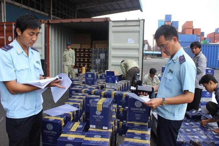 Vietnamese customs officers inspecting furniture in a shipping container, enforcing anti-fraud directive 17552 at a bustling cargo port with a container ship in the background.