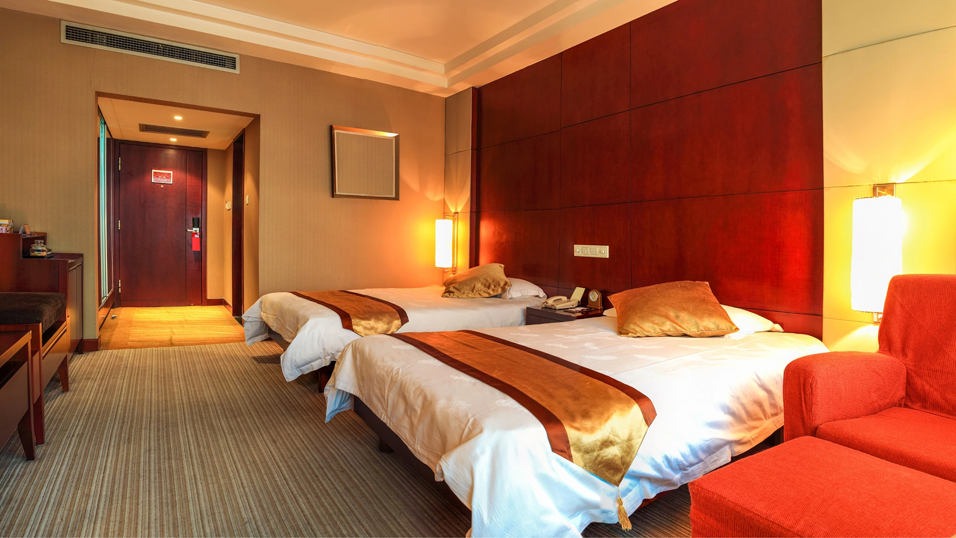 A sophisticated hotel suite bedroom showcasing a custom decorative headboard accent wall crafted from Premium Red Grandis™ quarter cut wood veneer by theShaper, displaying its signature elegant rosy-pink hue and perfectly straight linear grain.