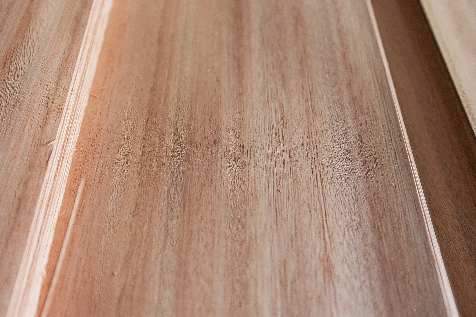 Close-up of Red Grandis wood veneer showing its natural, elegant warm rosy-pink and light reddish-brown coloration under studio lighting.