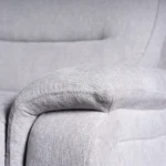 Close-up of deep-padded plush pillow-top armrest tailored in textured light grey fabric.